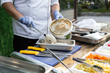 cook in blue gloves on the street puts hummus to prepare falafel in a metal box