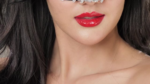 Macro closeup of Sexy woman wearing masquerade mask flirting at party over silver glitter background, slow motion.
