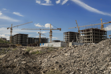 Buildings under construction. Kazakhstan (Ust-Kamenogorsk). Residential buildings. Construction cranes. Piles of stones. Cranes and buildings