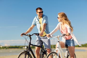 Obraz premium people, leisure and lifestyle concept - happy young couple riding bicycles on beach