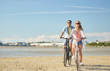 people, leisure and lifestyle concept - happy young couple riding bicycles on beach