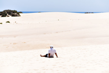 Man sitting on the sand dunes in Corralejo Natural Park in Fuertevantura Island, Canary Islands, Spain