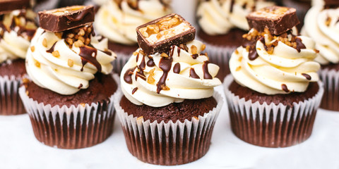 A lot of cupcakes with cream, chocolate and candy on top on a white background.