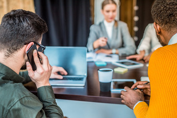 businessman talking by smartphone and using laptop in office