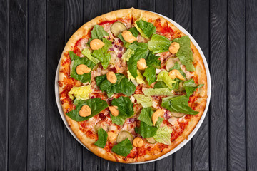 Top view of pizza with meat, pickled cucumber, onion, lettuce salad, tomato and barbecue sauce