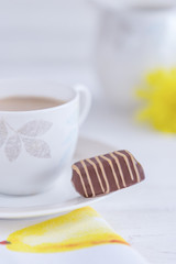 Porcelain cup of milk coffee and chocolate candy on a light background