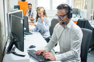 Young male technical support dispatcher with headset talking with customer in call center - obrazy, fototapety, plakaty