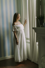 Young pregnant woman standing by the window