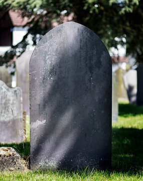 White marble gravestone (blank) in the shape of a cross. Trees and other graves in the background.