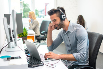 Attractive handsome young male customer service operator working on laptop in office