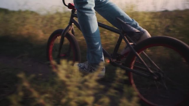 The bicyclist rides on his bmx outdoors at sunset. Slow motion close-up