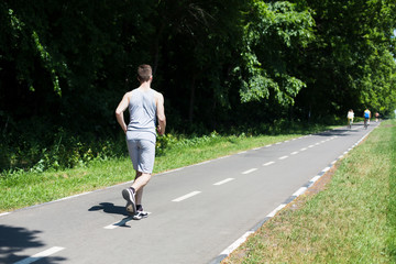 Fototapeta premium Young man jogging on treadmill in park, copy space