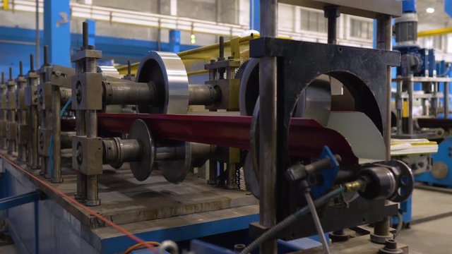 The machine cuts a sheet of metal. Factory for the creation of metal roofing. Rolling metal in the machine to create a metal roof.