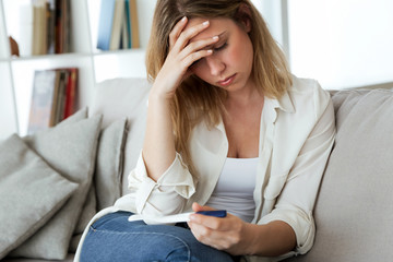 Young woman feeling depressed and sad after looking at pregnancy test result at home.