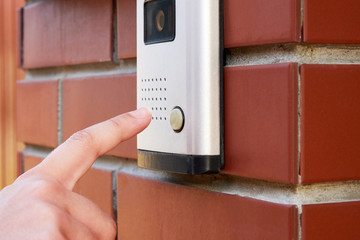 The female hand presses a button doorbell with intercom