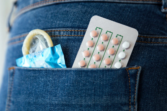 Woman with contraceptive pills and condom in the pocket of blue jeans.