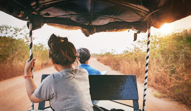 Point Of View Shot From Inside A Moving Tuk Tuk. The Passenger Ahead Looking Forward To The Road. Fast Driving On Rural Sandy Road Among The Fields At Sunset In Siem Reap, Cambodia