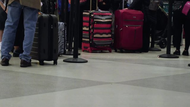 View of peoples legs as they wait in line at an airport terminal, and walk by with their luggage