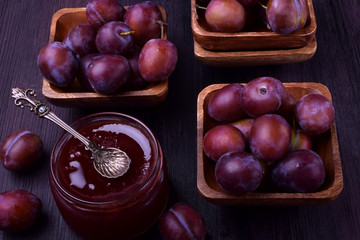 Plum jam in a glass jar surrounded by the berries