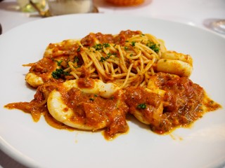 Closeup macro detail of a plate of squid seafood bolognese spaghetti with a glass of white wine at a table at an Italian restaurant, Paris, France. Travel and cuisine.
