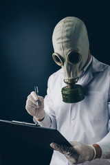 Creepy medical experiment concept, a scary doctor in gas mask holding a pen and clipboard on dark...