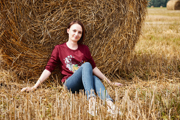 Naklejka na ściany i meble young girl having fun in the field, sits in a haystack and relaxing
