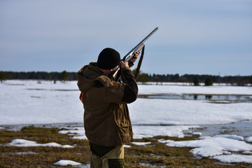The hunter with the gun is aiming at the game. Spring Hunt
