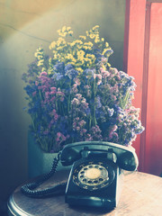 Beautiful Home Decoration of A Black Vintage or Old Fashioned Telephone on A Wooden Table with Colorful Dried Flowers in The Background.  Selective Focus and Blurred Background.