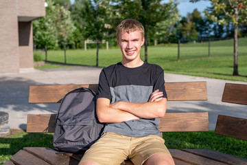 Obraz premium Happy teenager sitting on wooden bench that is next to a soccer/football field.