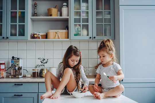 Two little girls in the kitchen sitting on the table.