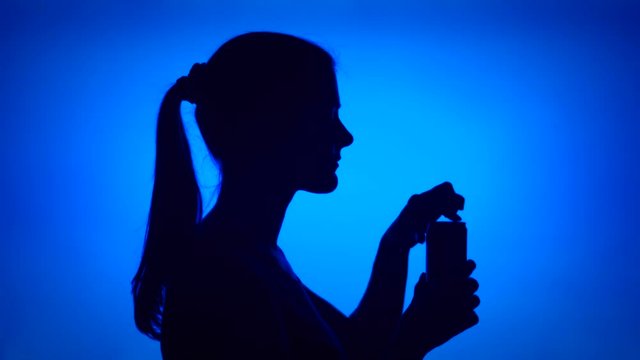 Silhouette of young woman opening can of soft drink on red background. Female's face in profile drinking soda from tin. Black contur shadow of teenager's half-face