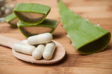 Fototapeta na wymiar closeup of sliced aloe vera leaves and pills in spoon on wooden background