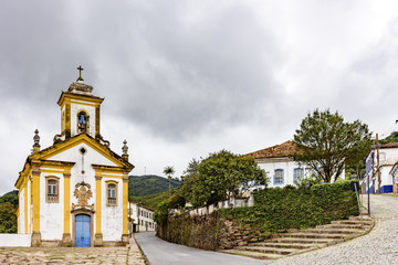Fototapeta na wymiar Ancient historical church, houases and streets in the brazilian historical city of Ouro Preto with dark clouds in background