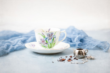 Royal Albert Iris Fine Bone China Tea Cup and Saucer with Herbal Tea and Tea Infuser on Blue Background