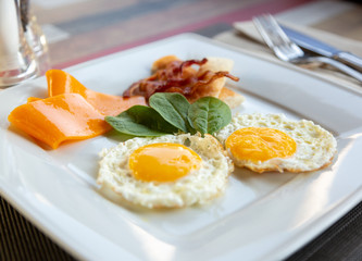 plate of fried eggs with bacon and vegetables on dark background, top view