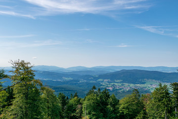 Fototapeta na wymiar View from top of a mountain in the valley with clouds on the sky and mountains on the background and trees in front of in the bavarian forest