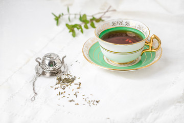 Royal Stafford Fine Bone China Tea Cup and Saucer with Loose Leaf Mint Tea, Spring of Fresh Mint in Background, and Tea Infuser on White Background