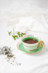 Royal Stafford Fine Bone China Tea Cup and Saucer with Loose Leaf Mint Tea, Spring of Fresh Mint in Background, and Tea Infuser on White Background