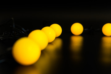 yellow glowing garland neatly straight-lined balls on a black background with light reflection