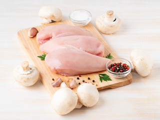 raw chicken breast fillet with spices on a wooden board on white wooden table, side view