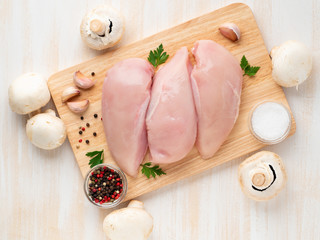 raw chicken breast fillet with spices on a wooden board on white wooden table, top view