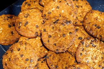 Chocolate chip cookies on rustic dark black background. Stacked chocolate chip cookies on brown napkin. Symbolic image with place for text. Freshly baked. Concept for a tasty snack. Sweet dessert