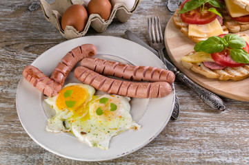 Fried eggs, sausages, sandwiches with cheese, tomato and basil