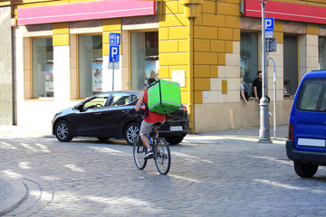 Mężczyzna na rowerze z zielonym kufrem, plecakiem na plecach. - obrazy, fototapety, plakaty