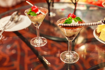 Selective focus of Chocolate creamy trifle in beautiful cocktail glasses with fresh red ripe cherry fruit and chocolate spiral stick topping on table background. Delicious Healthy dessert concept