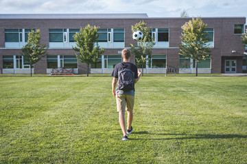 Teenager tossing a soccer ball in the air as he walks through an empty soccer field.
