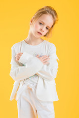 A teenage girl in white clothes posing on a yellow background. The girl lowered her jacket to her elbows.