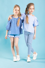 Girls twins in light blue clothes are posing on a blue background.