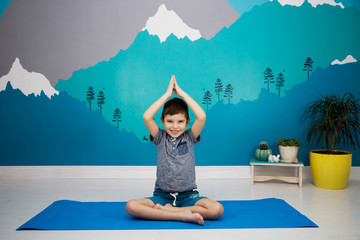 Cute caucasian boy does yoga in his room with a beautiful mountain mural. Anjali Mudra, namaste,...