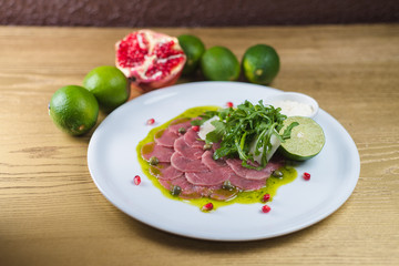 Carpaccio with Parmesan, lime and pesto sauce, on a white plate